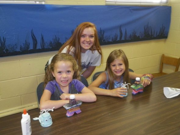 Karaline Graham, 6, and Kylee Bice, 7, show off the crafts they made with the help of their junior leader, Grace Miller, at the Cloverbud Day Camp held at Grace UMC on June 17. 