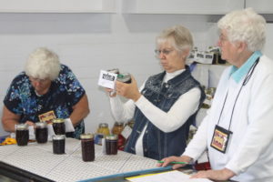 Vicki Bechtel, center, carefully exams canned goods during judging on Sept. 28 in the art hall at the Coshocton County Fairgrounds. Josie Sellers | Beacon