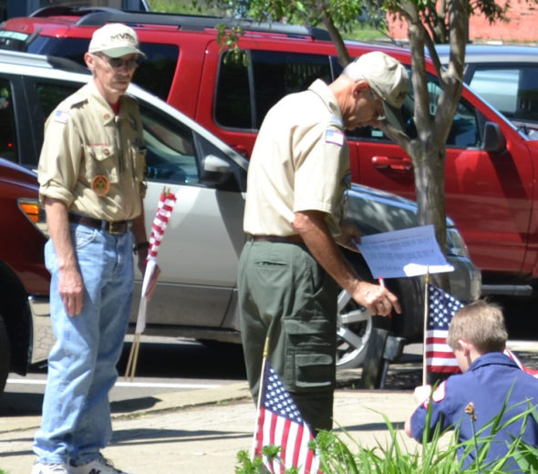 A Boy Scout is pictured placing a flag on the Coshocton Court Square as the name of a veteran who passed away in the last year was read during the Coshocton Memorial Day Service. Jen Jones | Beacon